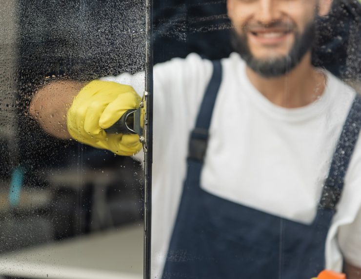 cropped view of smiling cleaner washing window in office