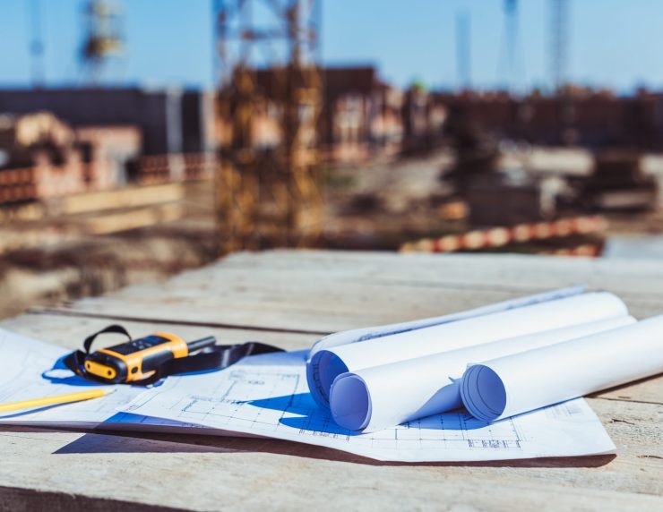 Rolls of paper with building plans and portable radio on wooden surface at construction site